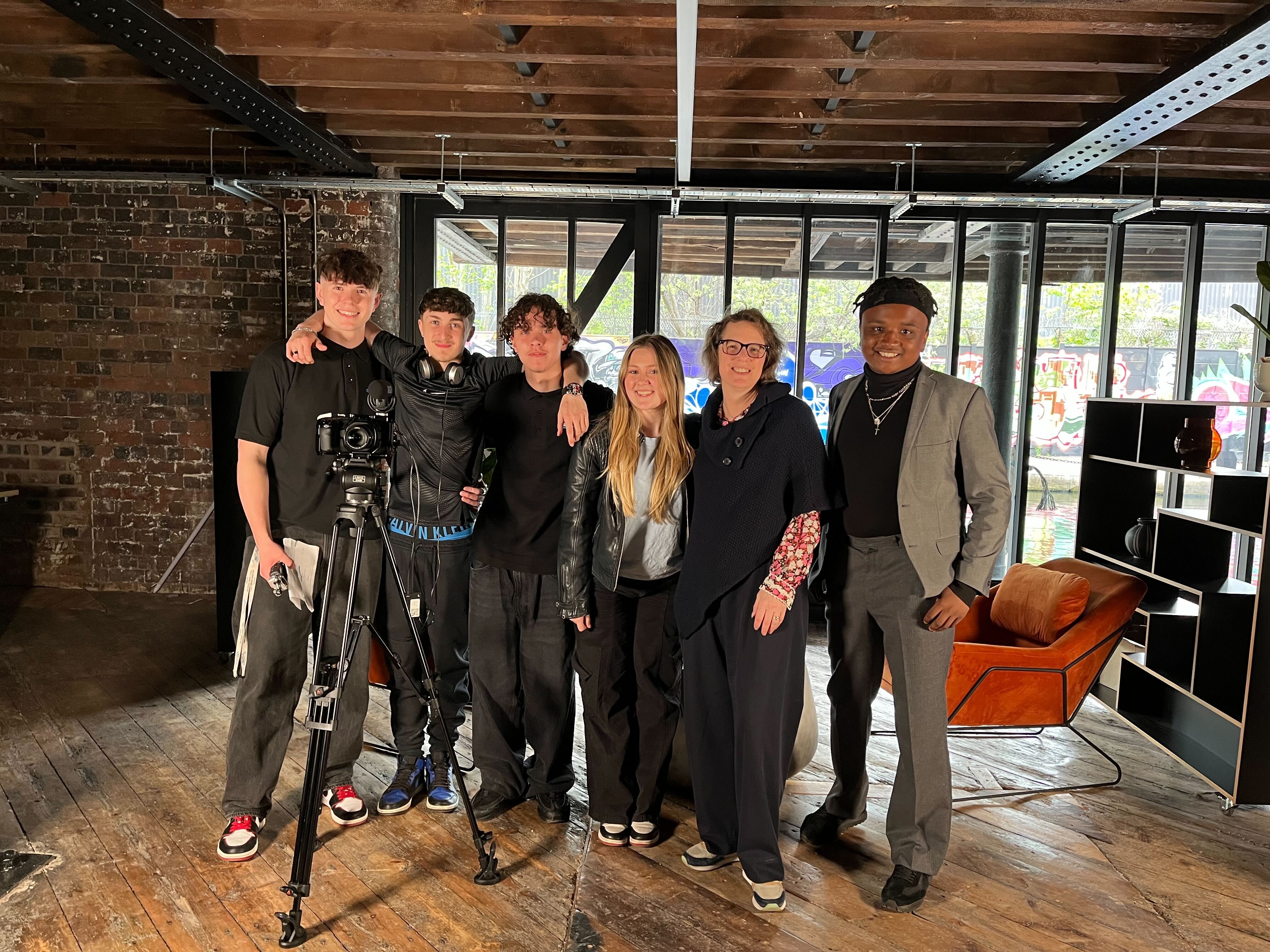 A group of students stood in a line smiling with a camera and Alison grade.